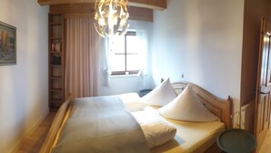 A bedroom with a large bed, a bedside table, a window with curtains, and a bookshelf. - Vacation apartment with terrace, garden and lake view on the ground floor, for 2 to 3 pers. (Waging am See)