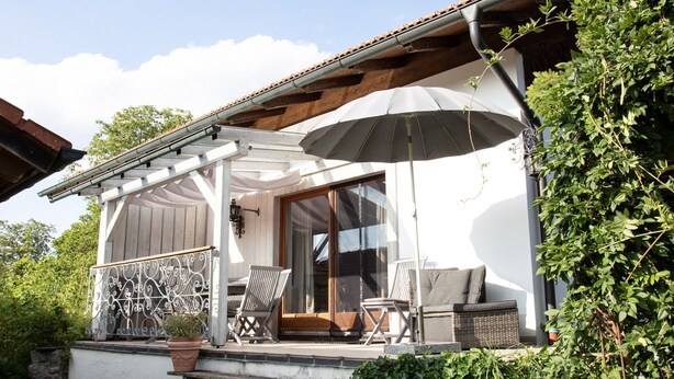 A covered outdoor seating area with two chairs and a table, a pergola, and a large umbrella. - Vacation apartment with terrace, garden and lake view on the ground floor, for 2 to 3 pers. (Waging am See)