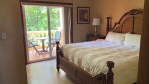 Une chambre à coucher avec un grand lit, une table de chevet, une lampe et une vue sur un balcon aménagé avec du mobilier d’extérieur.