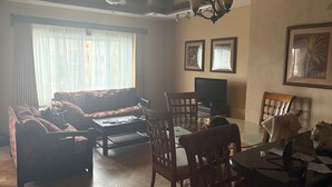 Un salon comprenant un canapé, des fauteuils, un téléviseur et une table à manger.