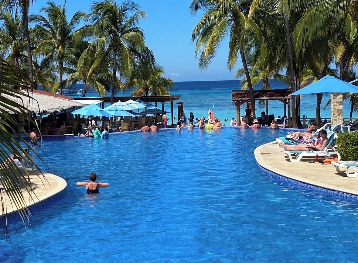 Área de piscina com palmeiras, espreguiçadeiras e guarda-sóis.