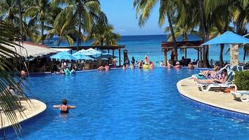 Área de piscina com palmeiras, espreguiçadeiras e guarda-sóis.