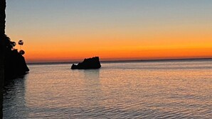 Vista de un atardecer costero con aguas tranquilas y una formación rocosa distante.