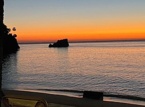 A coastal sunset view with calm waters and a distant rock formation.