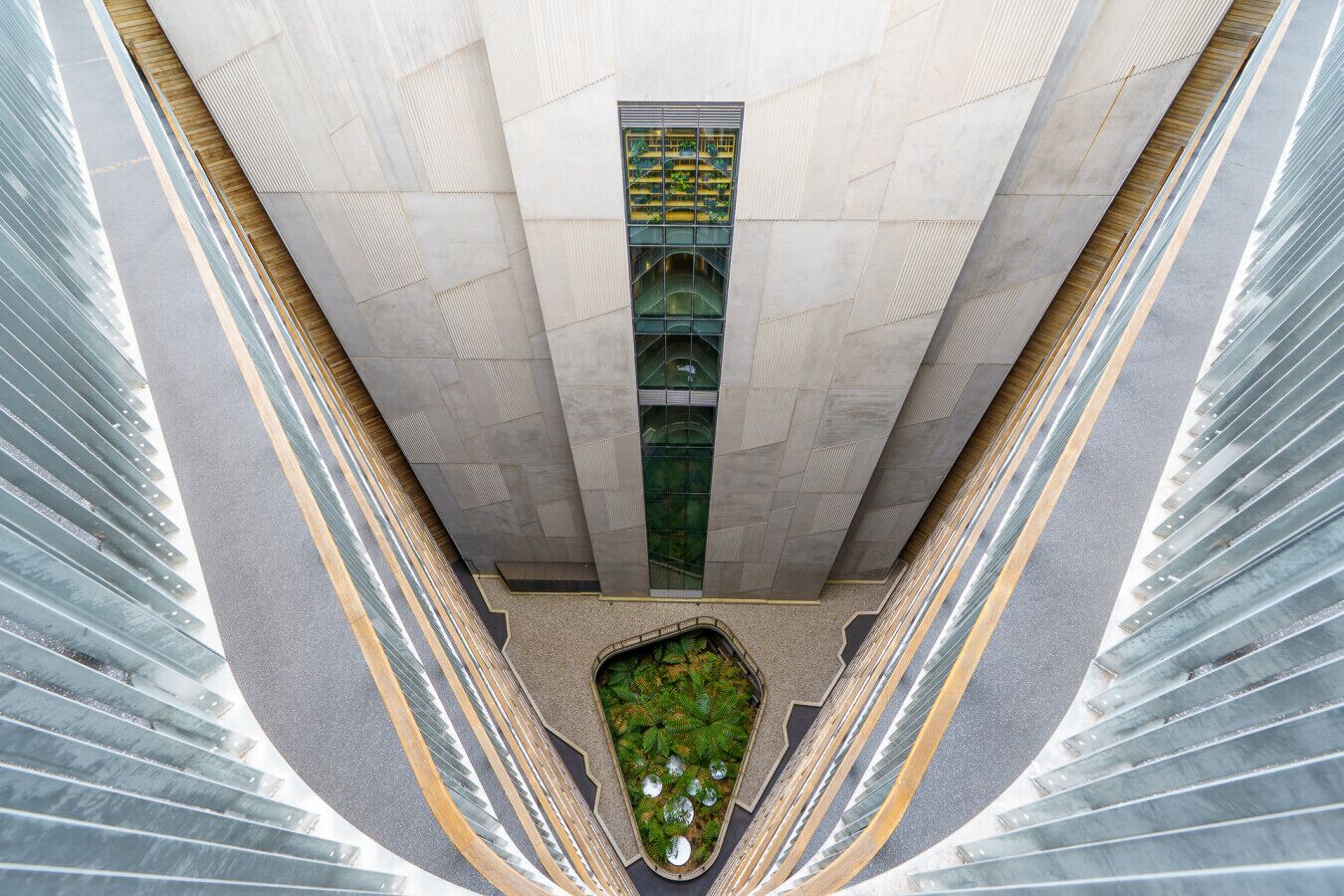A high-rise building with a central atrium, large windows, and a small garden area at the base.