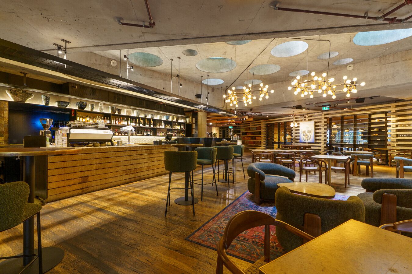 A modern bar area with a wooden counter, bar stools, and a seating area with tables and chairs.