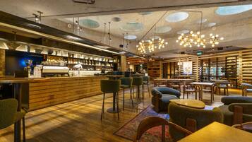 A modern bar area with a wooden counter, bar stools, and a seating area with tables and chairs.
