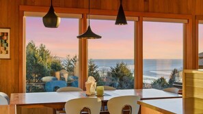 A dining area with a view of the ocean, wooden walls, and pendant lights. - Sea to Sky Retreat by Manzanita Beach Getaway: Ocean Views, 3BR Hilltop Home (Nehalem)