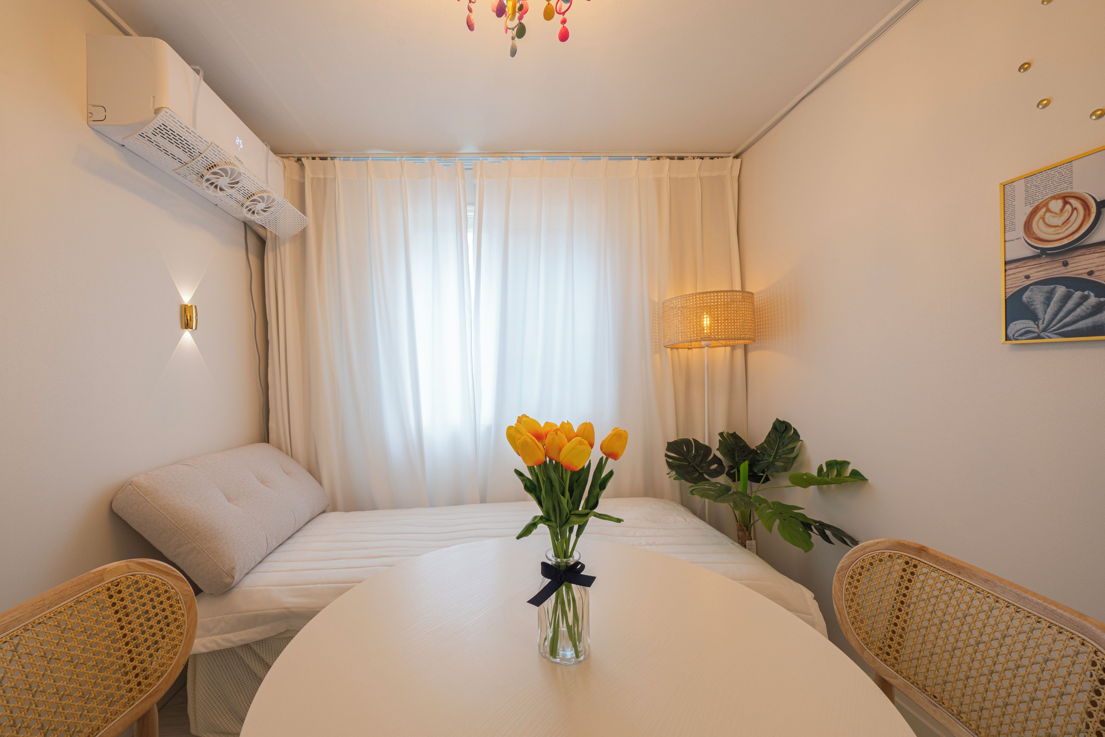 Habitación de hotel con cama, una mesa con un florero, una silla, una lámpara y aire acondicionado instalado en la pared.
