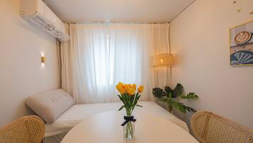 Habitación de hotel con cama, una mesa con un florero, una silla, una lámpara y aire acondicionado instalado en la pared.