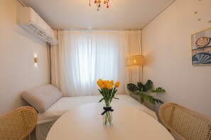 A hotel room with a bed, a table with a vase of flowers, a chair, a lamp, and a wall-mounted air conditioner. - Golden Stay (Busan)