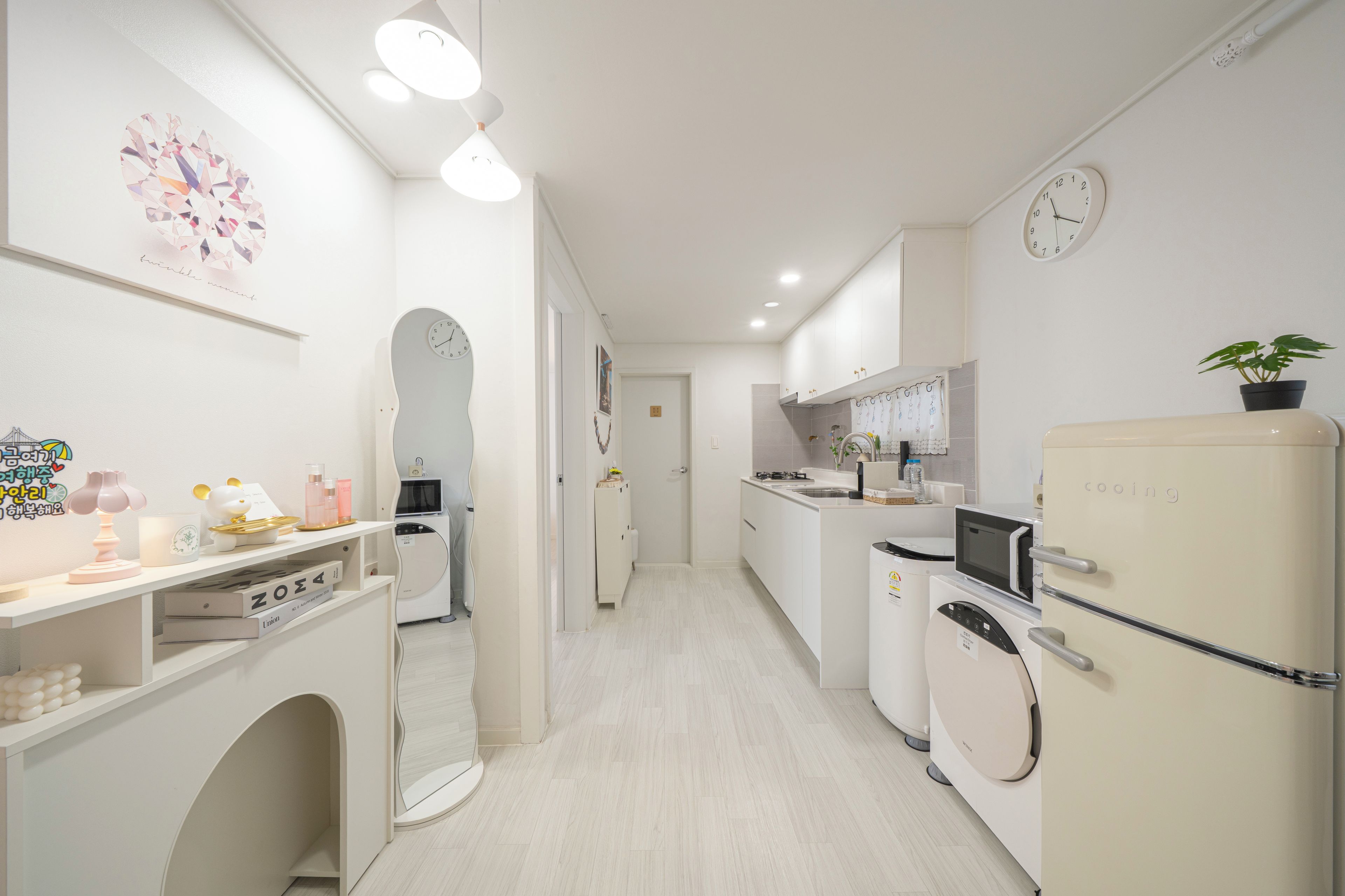 Une cuisine moderne avec des appareils électroménagers blancs, un four à micro-ondes et un réfrigérateur. On y trouve un évier, un plan de travail avec un miroir et une horloge au mur.