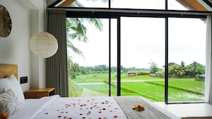 A bedroom with a large bed, a view of green fields, and a wooden headboard. - Dzen Greenfield Villa 9 (Ubud)