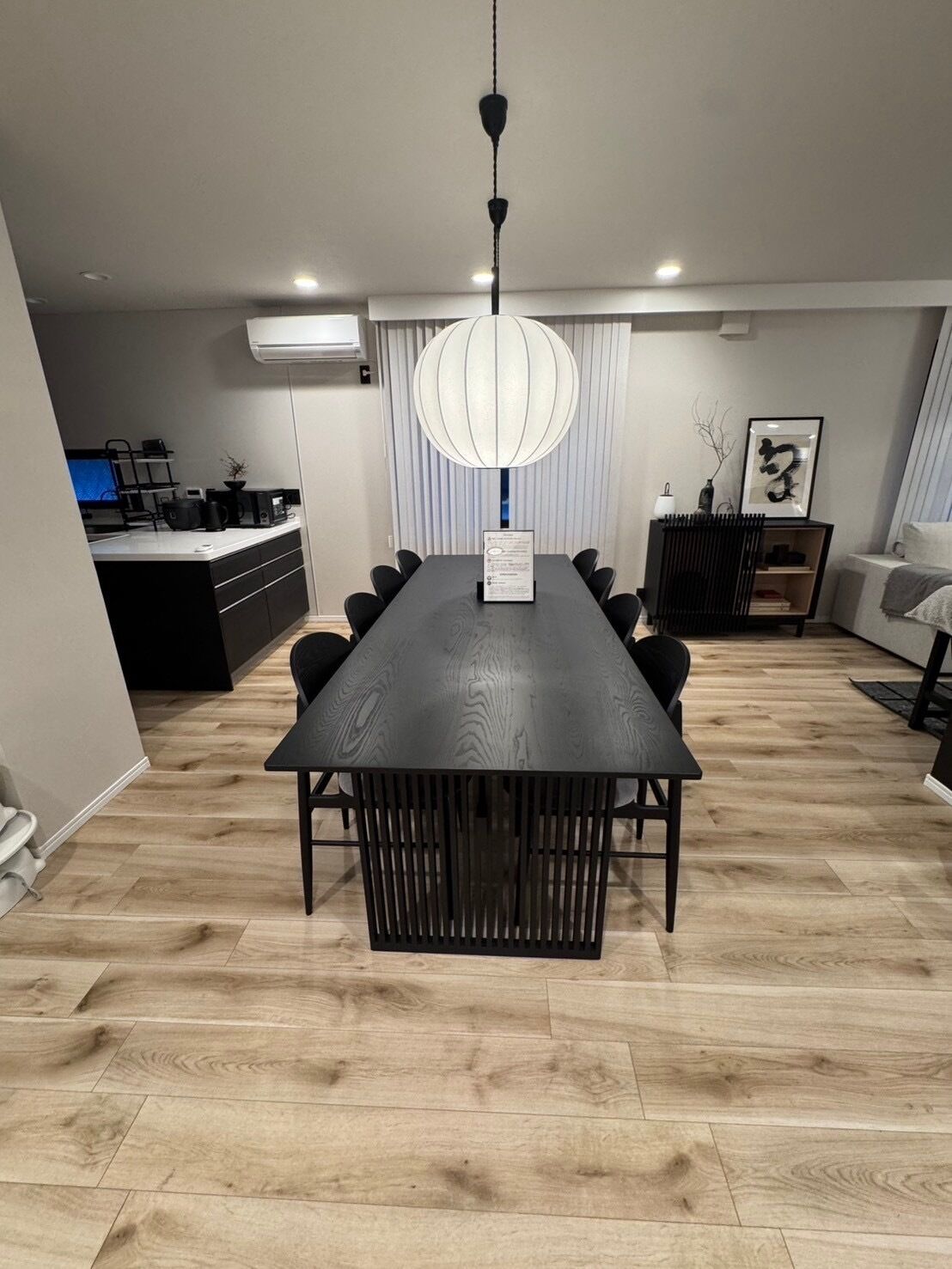 A modern dining area with a long table, black chairs, and a hanging light fixture.