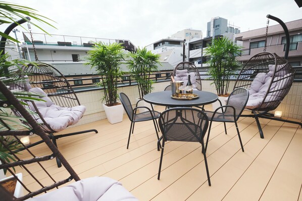 Una terraza en la azotea con una mesa redonda, sillas de metal negro y plantas en macetas.