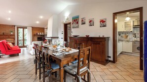 Un coin repas avec une table et des chaises en bois, un canapé rouge et une cuisine dotée de meubles blancs et d’un réfrigérateur bleu.
