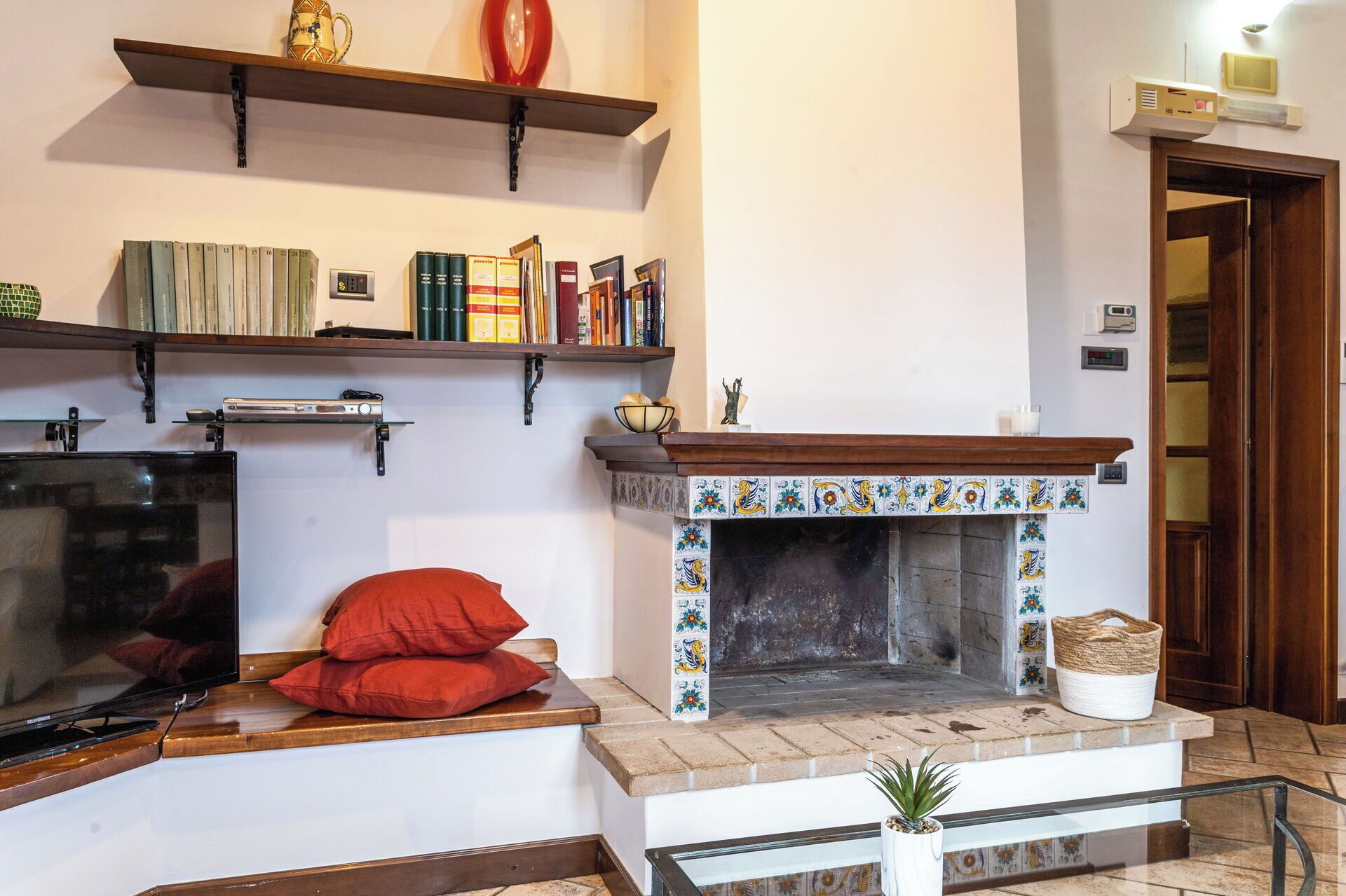 A living room with a fireplace, bookshelves, a television, and a red sofa.