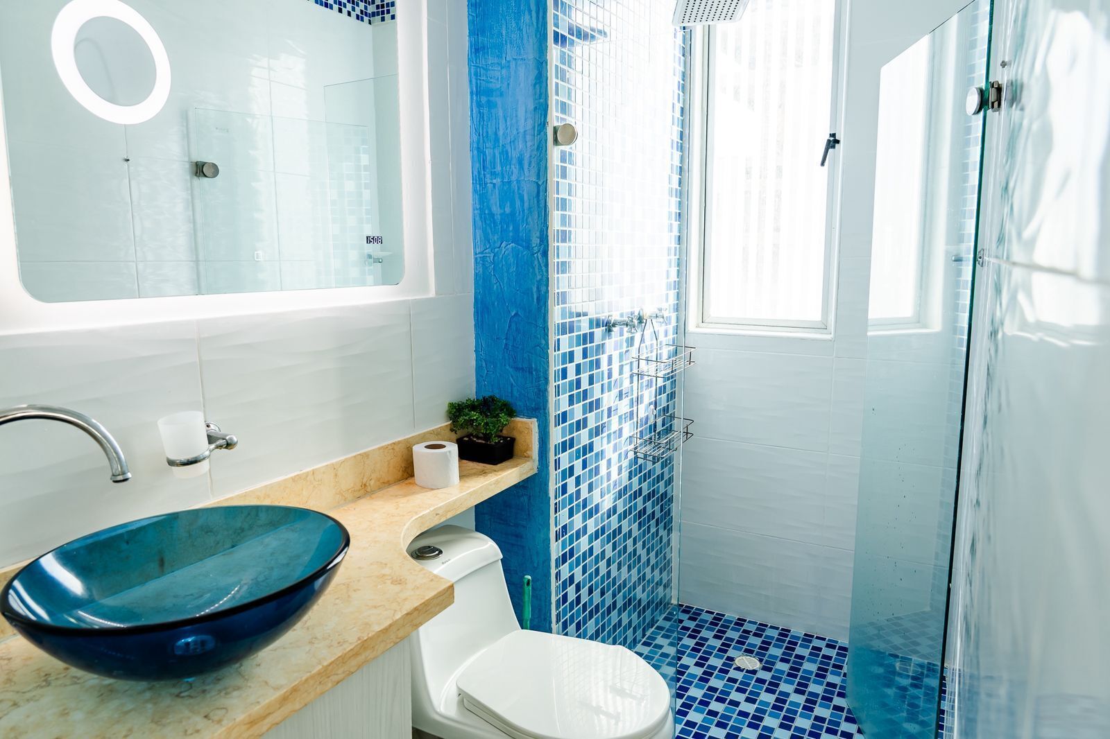 A bathroom with a blue-tiled shower, a white toilet, and a blue bowl sink.