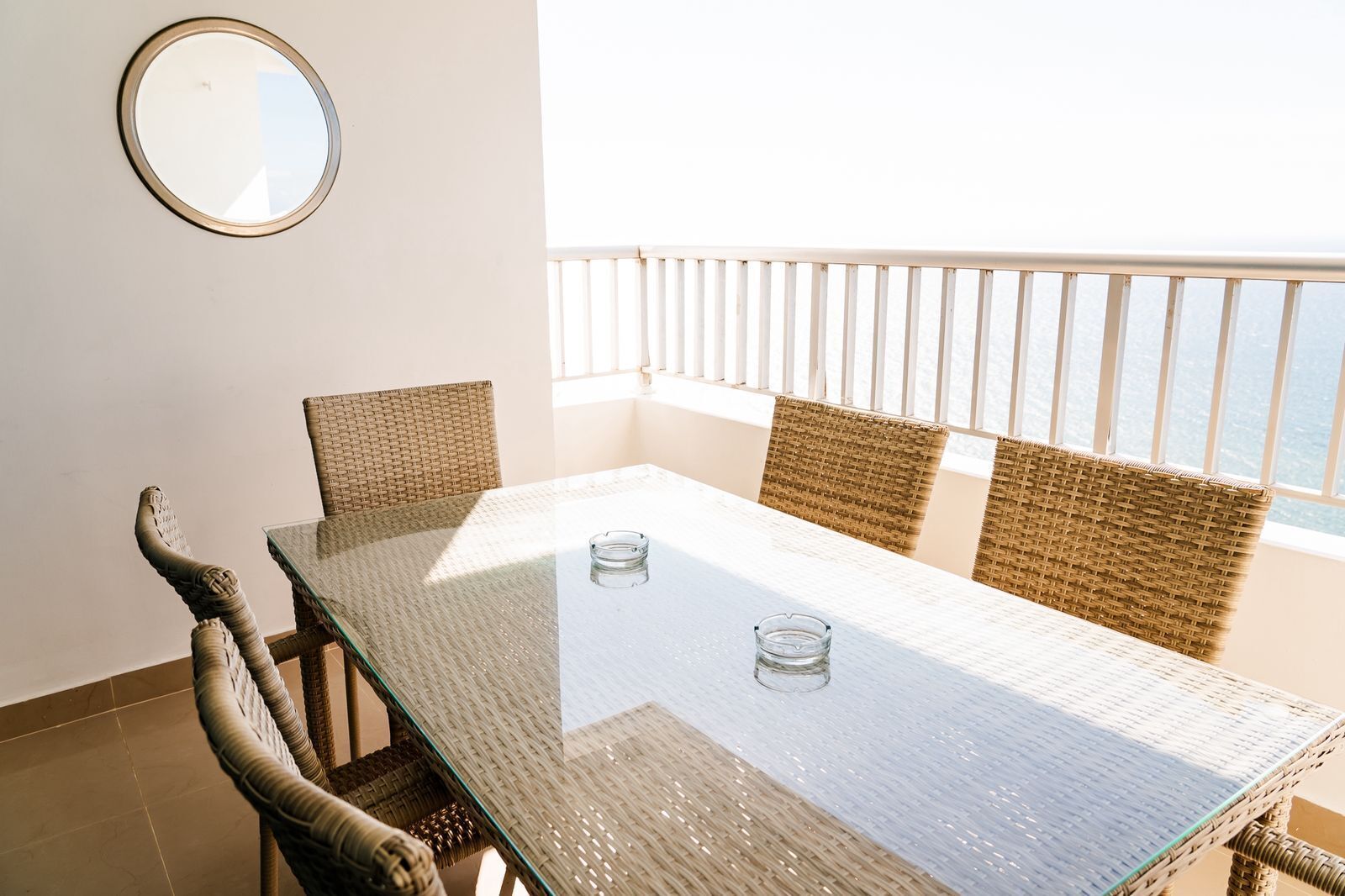 A balcony with a table and wicker chairs, overlooking a body of water.