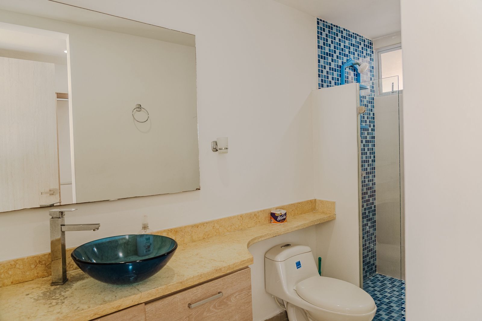 A bathroom with a blue glass basin, a white toilet, and a shower area with blue tiles.
