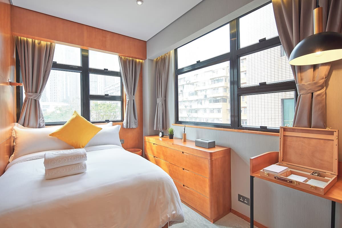 Una habitación de hotel moderna con una cama grande, un aparador de madera y un escritorio con lámpara.
