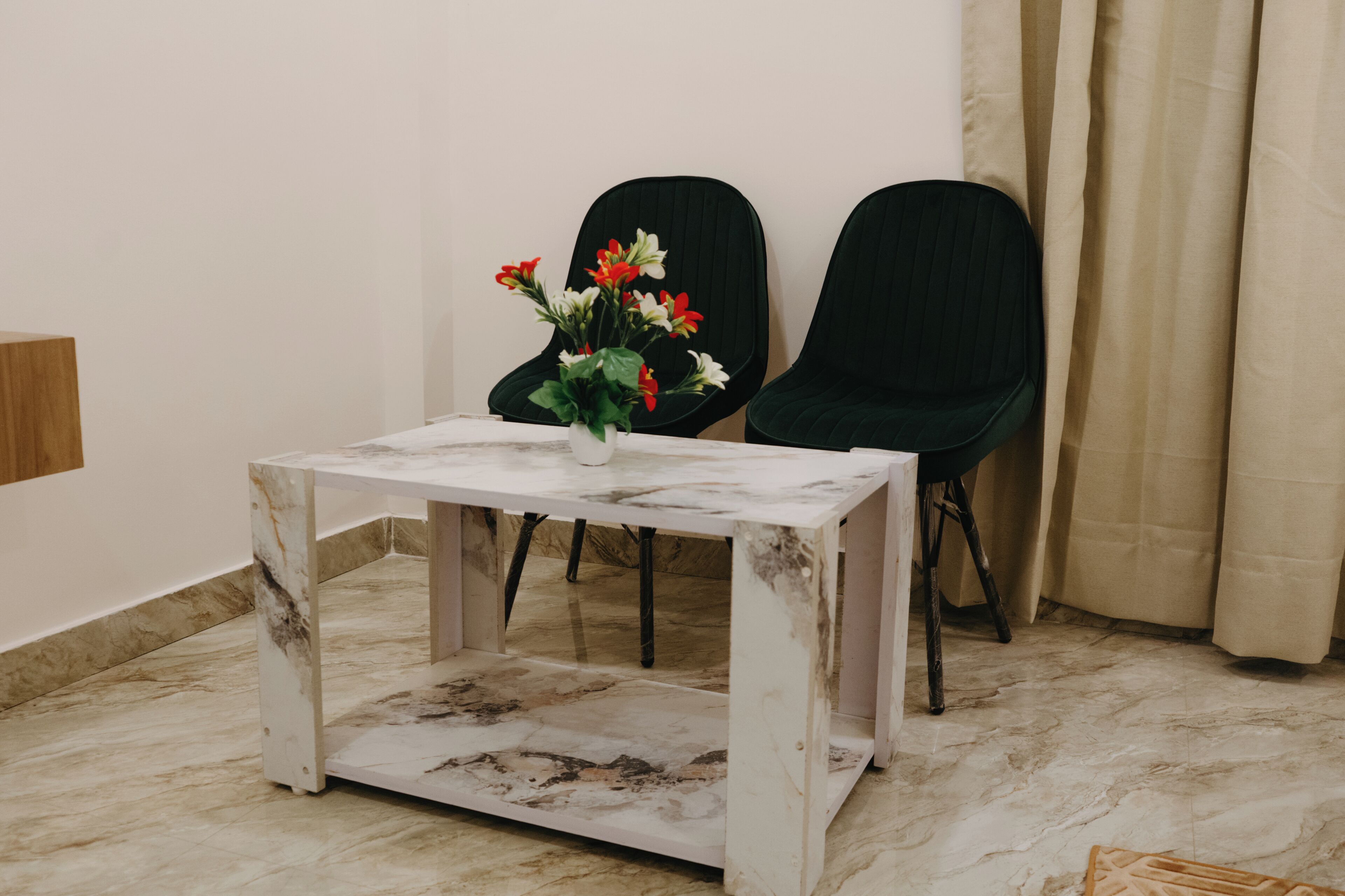 Ein Zimmer mit einem Tisch aus Marmor, zwei schwarzen Stühlen, einer Vase mit Blumen und einem Vorhang.