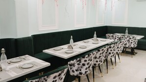 A dining area with a long table set for multiple guests, surrounded by green upholstered booths and floral-patterned chairs. - The Manthan Hotel - City View (Faizabad)