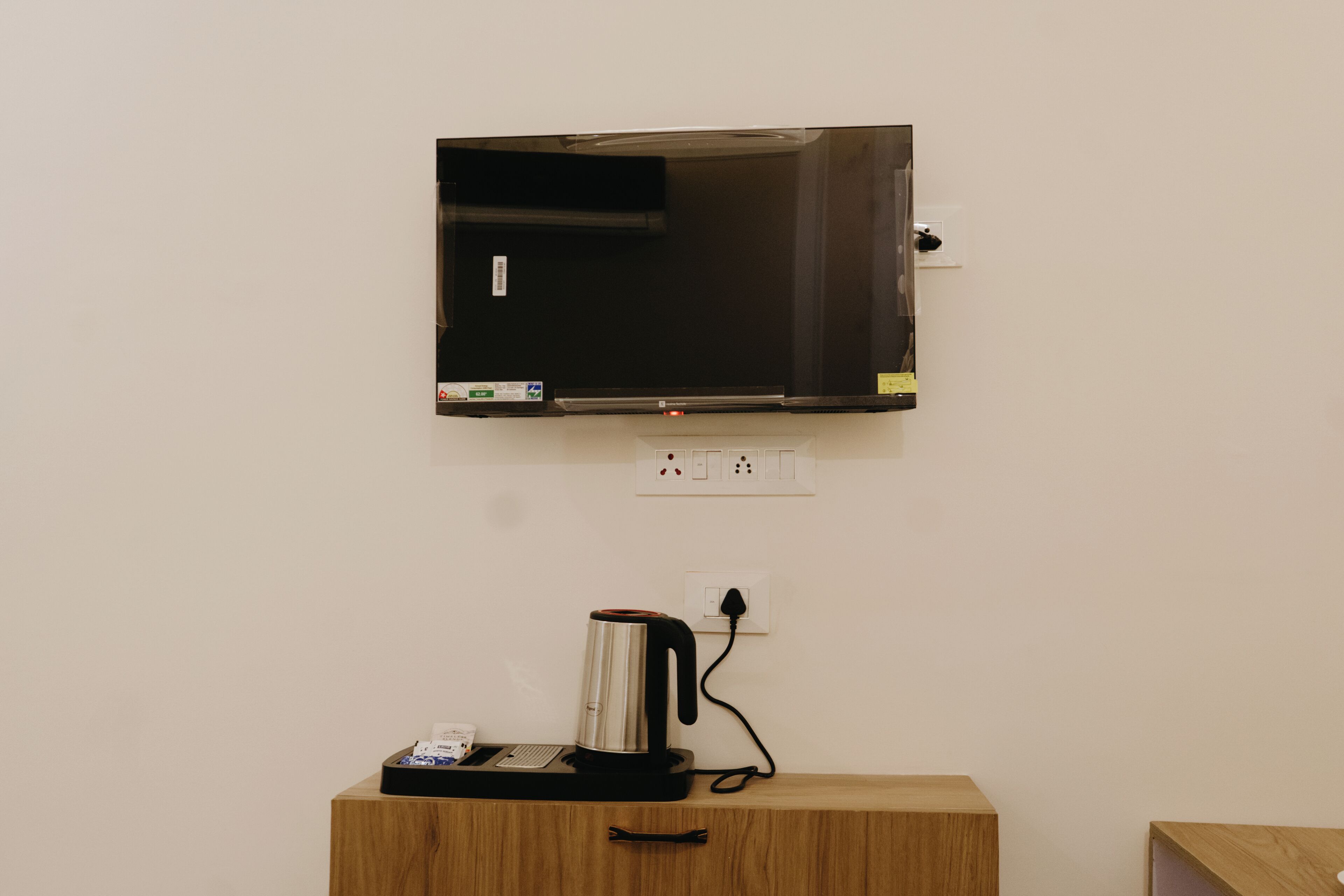 A flat-screen TV mounted on a wall above a wooden cabinet with a coffee maker on it.