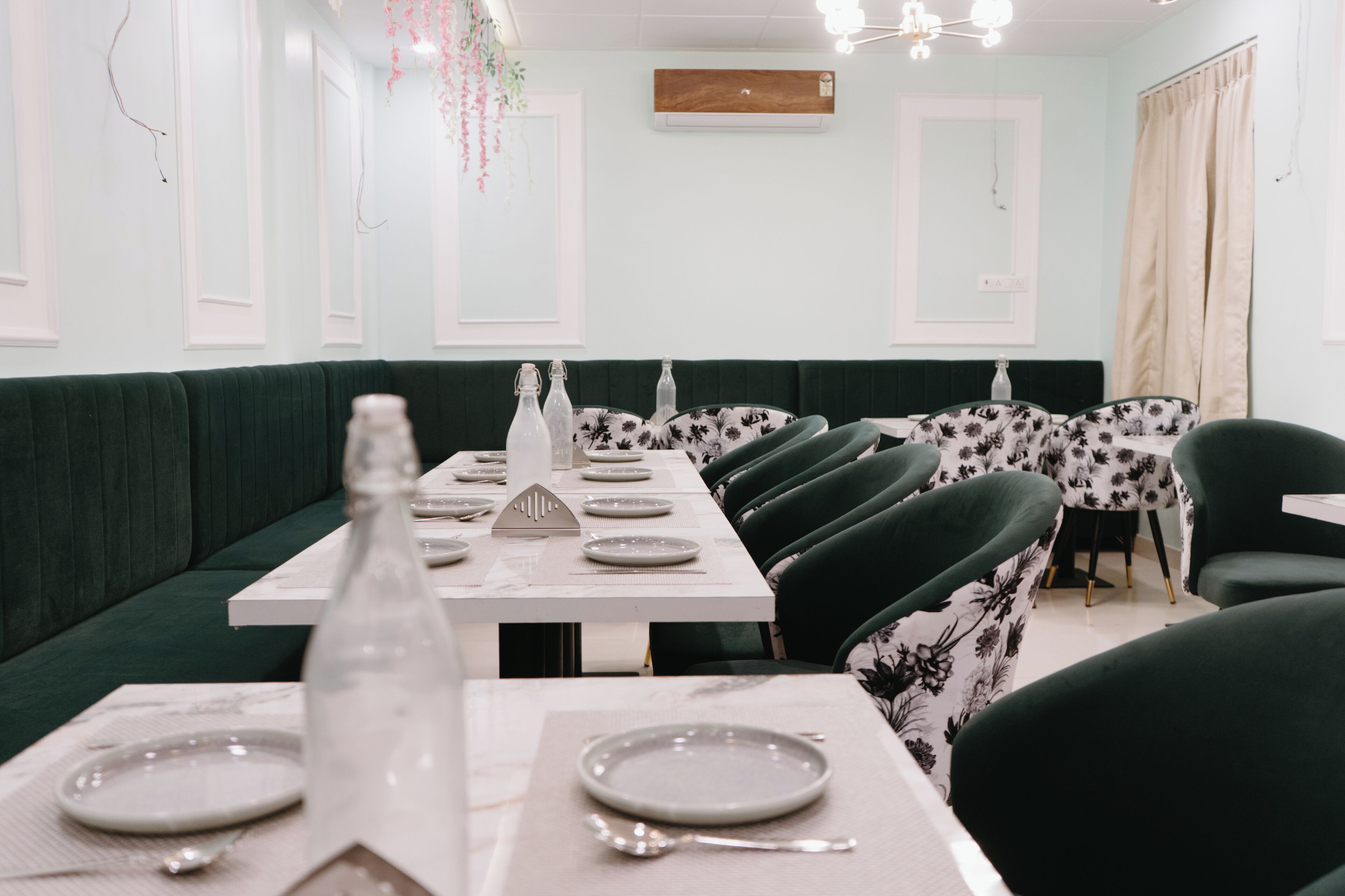 A dining area with green upholstered booths, white tables, and floral-patterned chairs.