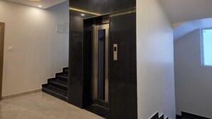 A modern interior with a staircase leading to a dark elevator, recessed lighting, and a plain wall. - The Manthan Hotel - City View (Faizabad)