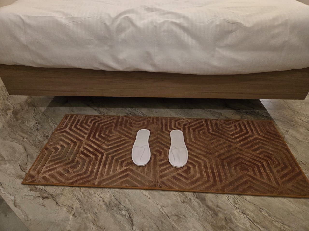 Un lit avec un matelas blanc et un tapis à motifs marron en dessous.