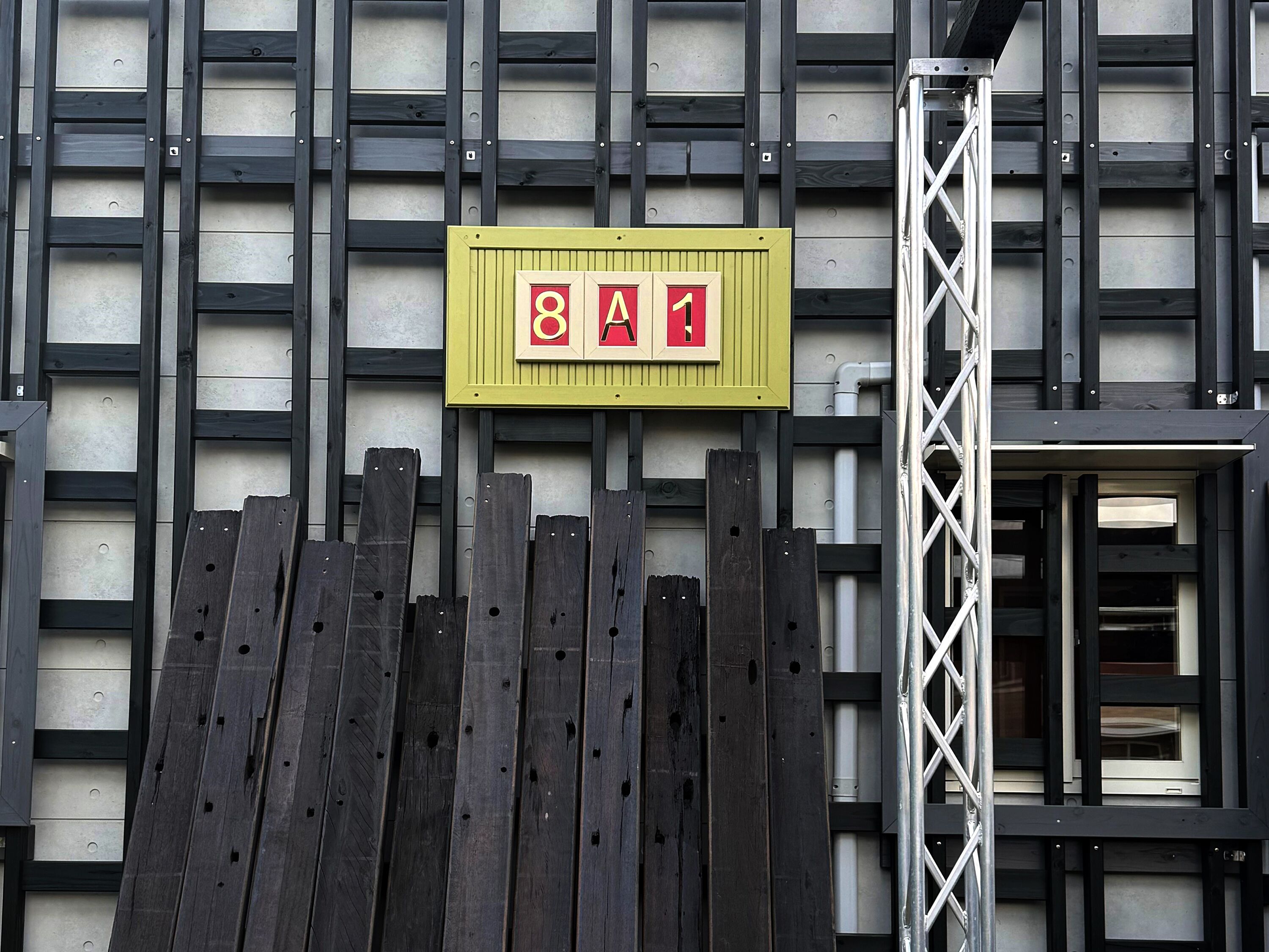 A building facade with a yellow sign with red and white letters spelling '8A1' and a metal scaffolding structure to the right.