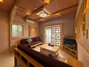 A cozy living room with a sofa, a coffee table, a TV, and a decorative screen door. - Yufuin Onsen 8A1 Yaeichi (Yufu)