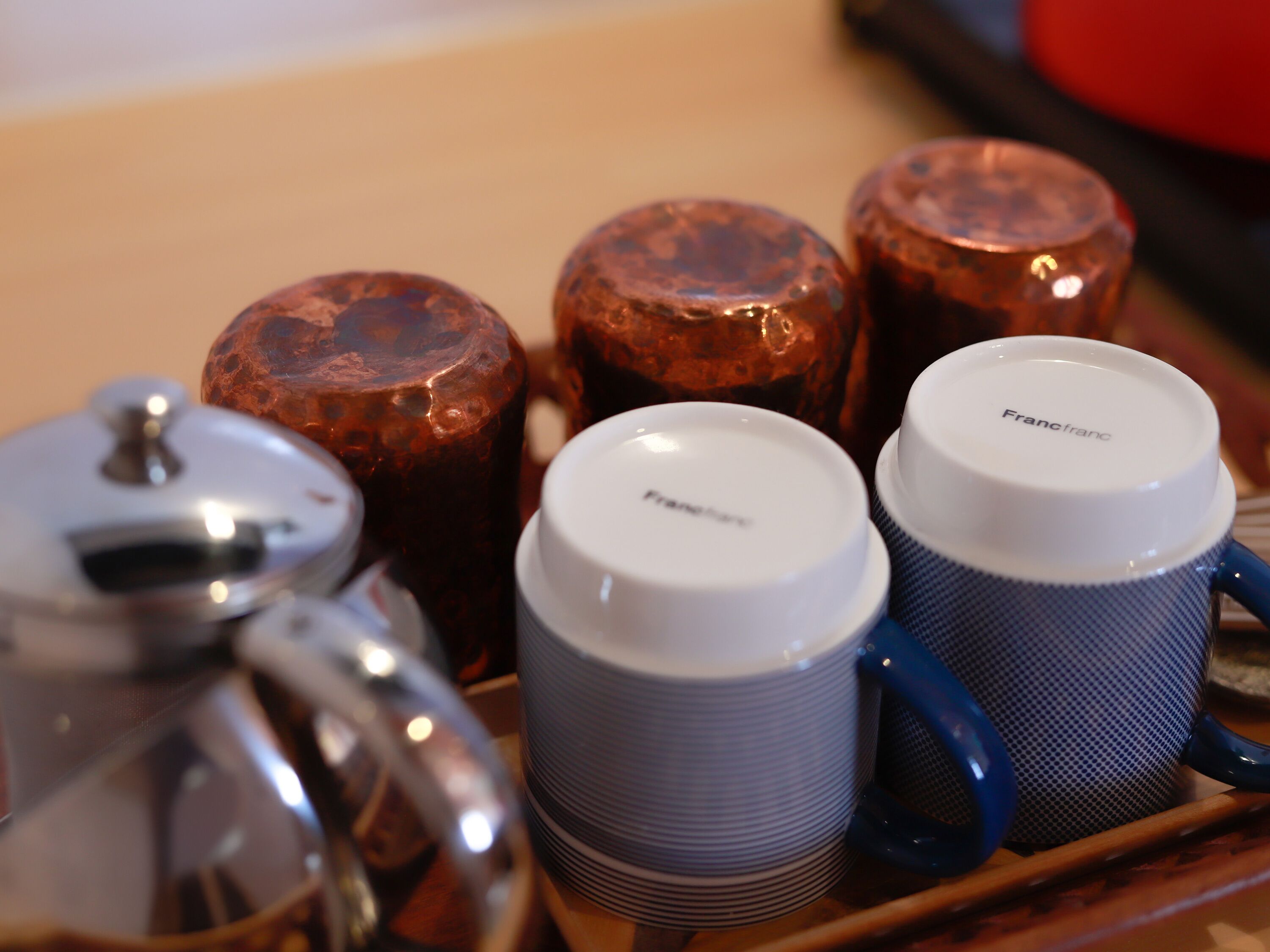 Una bandeja con un hervidor de agua, dos tazas blancas y tres vasos de cobre.