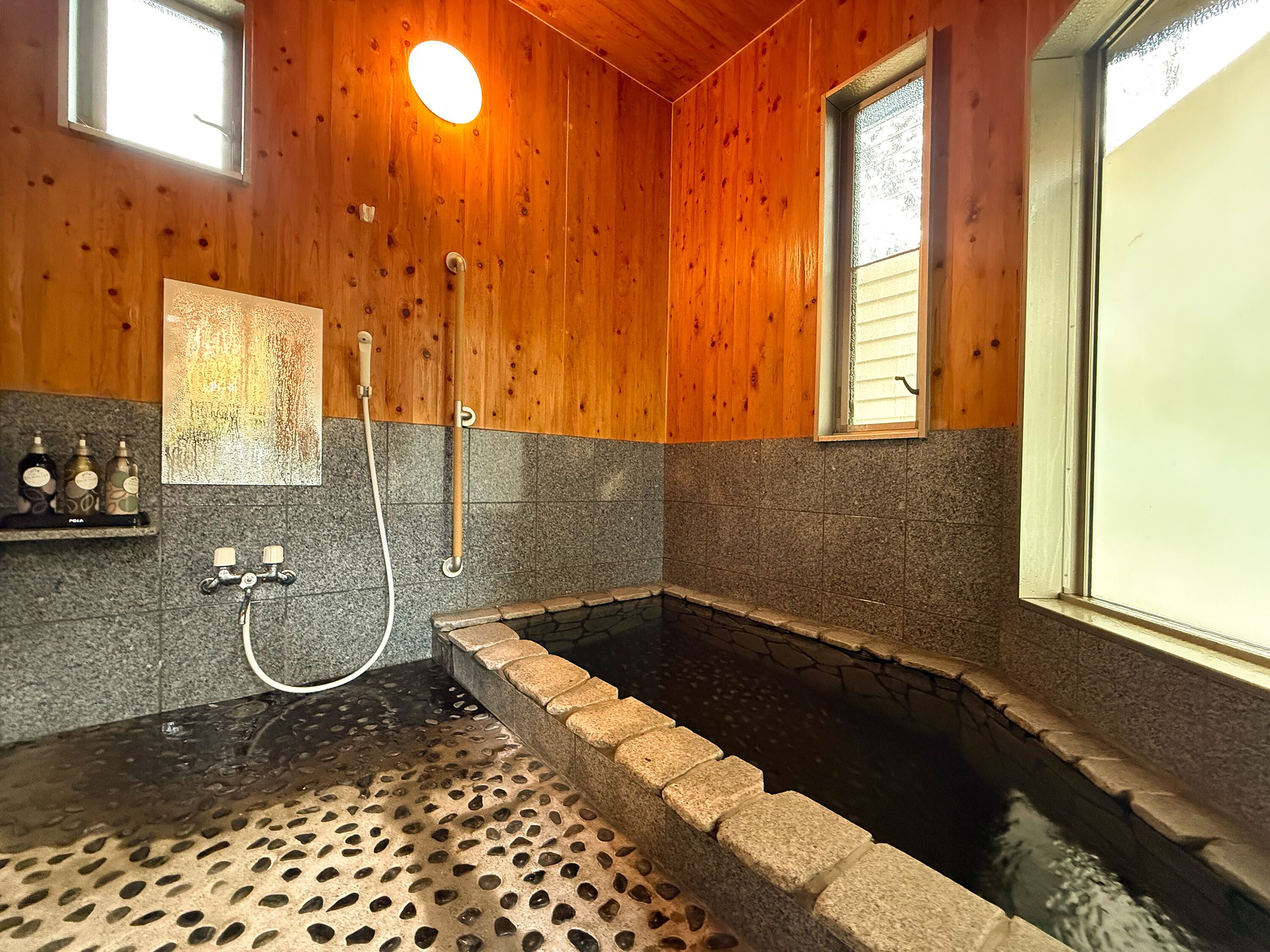 A wooden interior with a stone-tiled shower area and a small window.