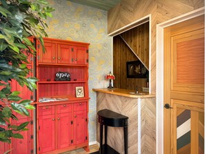 Ein Zimmer mit einem roten Schrank, einem kleinen Hocker, einem an der Wand befestigten Regal mit Dekorationen und einer Holztür.