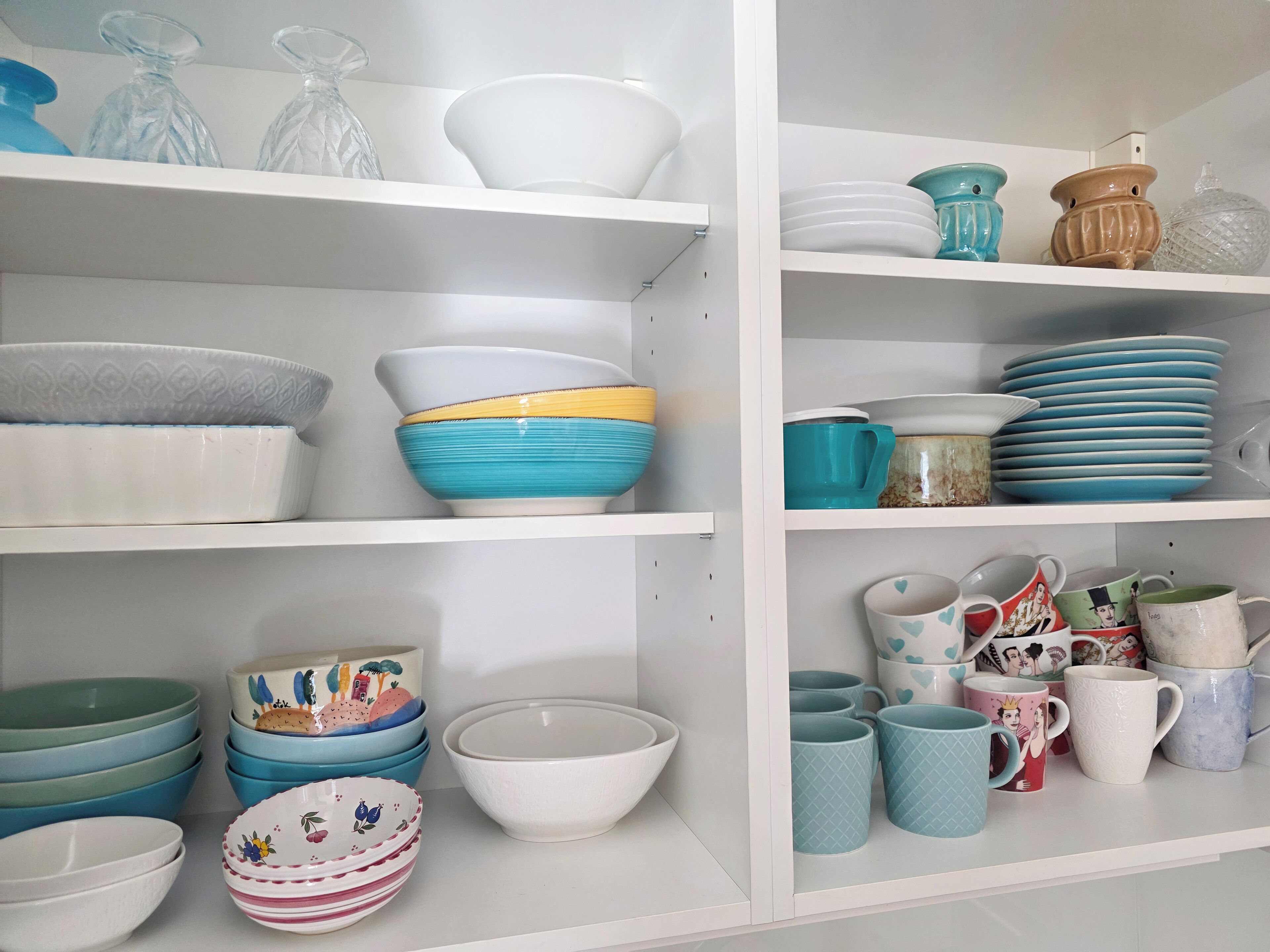A kitchen with white shelves holding various bowls, plates, and mugs.