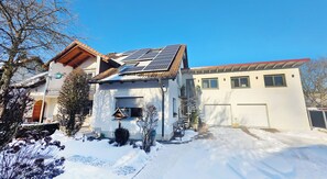 A two-story house with solar panels on the roof, a garage, and a snow-covered driveway.