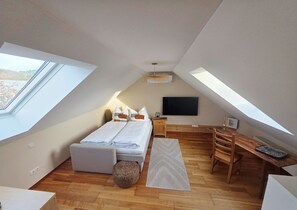 A bedroom with a bed, bedside table, TV, wooden desk, chair, and a small round ottoman. - Modern, well-maintained, and cozy vacation apartment in Donaustauf near Regensburg, 3.5 bedrooms (Donaustauf)
