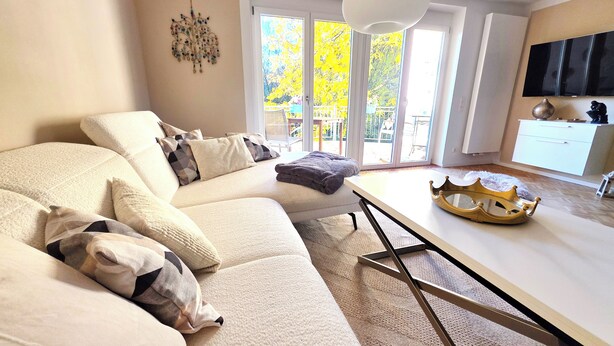 A modern living room with a beige sofa, a white coffee table, and a large window with a view of trees. - Modern, well-kept and cozy vacation apartment in Donaustauf near Regensburg 3 bedrooms (Donaustauf)