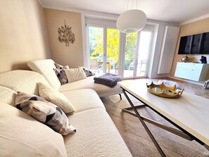 A modern living room with a beige sofa, a white coffee table, and a large window with a view of trees. - Modern, well-maintained, and cozy vacation apartment in Donaustauf near Regensburg, 3.5 bedrooms (Donaustauf)