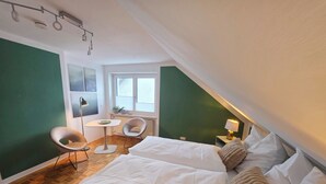 A modern hotel room with a large bed, a small table, two chairs, a window, and a ceiling light fixture. - Modern, well-kept and cozy vacation apartment in Donaustauf near Regensburg 3 bedrooms (Donaustauf)
