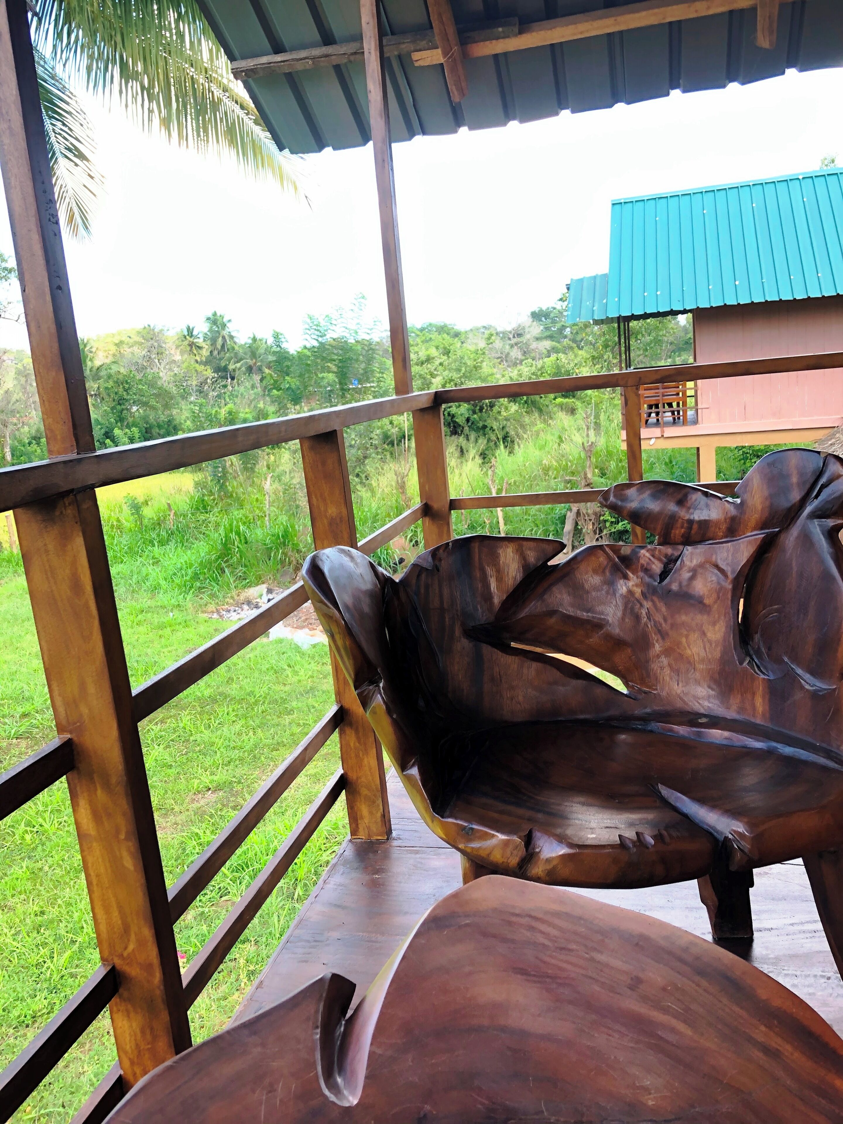 A wooden bench and table under a covered area with a view of a lush green landscape and a building with a blue roof.