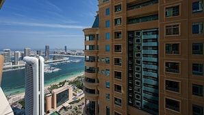 Ein Hochhaus mit mehreren Etagen und Balkonen, das auf eine Marina und einen Strand blickt.