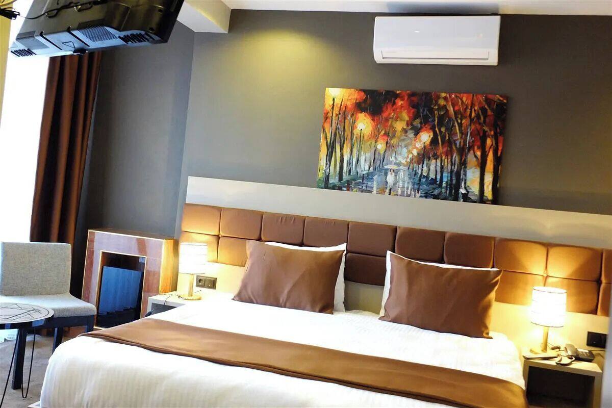 Une chambre d’hôtel avec un grand lit, deux lampes de chevet, un tableau au mur et un téléviseur fixé au-dessus du lit.