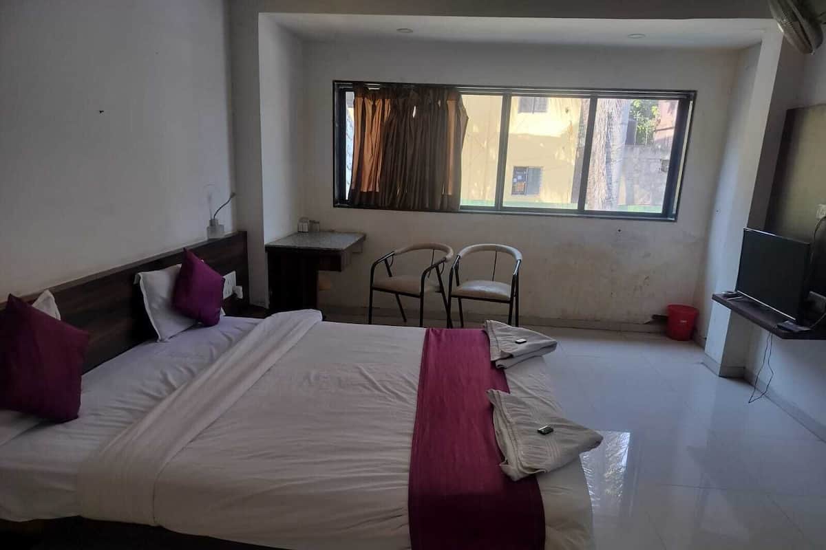 A hotel room with a large bed, a desk, two chairs, a TV, and a window with curtains.
