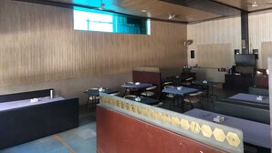 A modern indoor space with wooden panel walls, a reception desk, multiple tables and chairs, ceiling fans, and a television. - Hotel Saiba Lodging  (Paud)