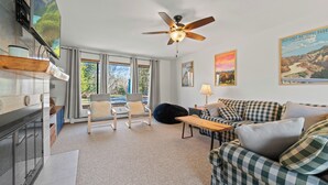 Ein Wohnzimmer mit einer Couch, Sesseln, einem Deckenventilator und einem an der Wand befestigten Fernseher.