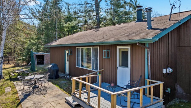 Eine Holzhütte mit Terrasse, überdachter Veranda und kleinem Tisch mit Stühlen im Freien.