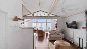 Un vaste espace de vie doté d’un haut plafond, d’un ventilateur de plafond, d’un téléviseur fixé au mur et d’une grande fenêtre offrant une vue sur l’extérieur.